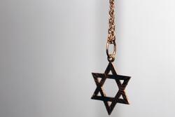 Gold Star of David necklace hanging in midair, in partial focus.